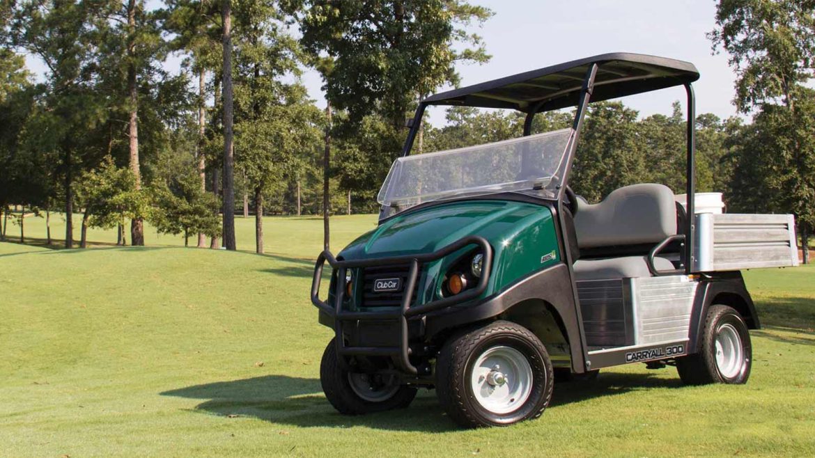 A photo of a Club Car Carryall 300 utility vehicle on a golf course with trees in the background.