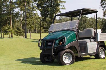 A photo of a Club Car Carryall 300 utility vehicle on a golf course with trees in the background.