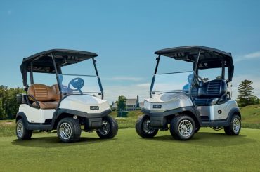 A photo of two Club Car Temp golf carts on a golf course green standing and three-quarter view and nose to nose.