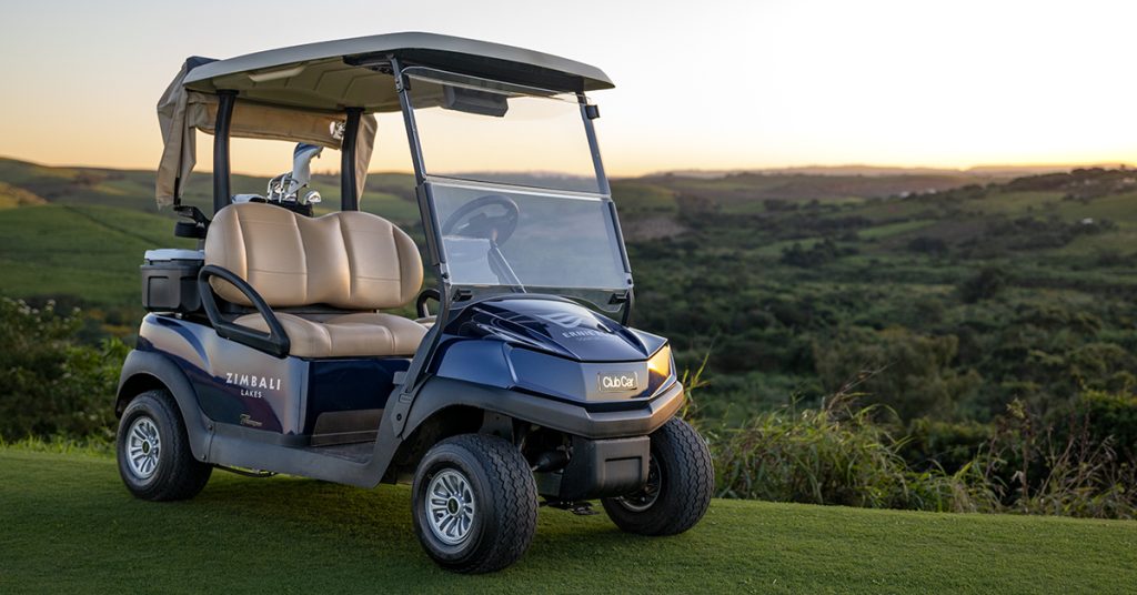 A blue Club Car Tempo parked on a golf course with a sunset behind it.