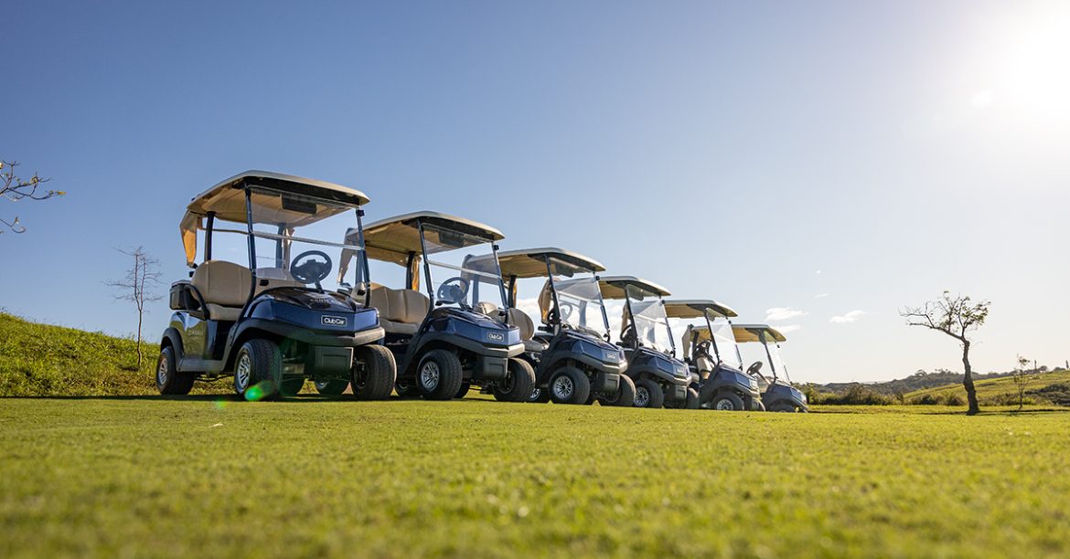 A fleet of blue Club Car Tempo standing in a row on a golf course.