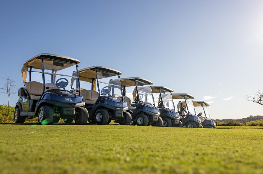 A fleet of blue Club Car Tempo standing in a row on a golf course.