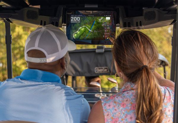Two people in a Club Car golf cart making use of the Club Car Connect to navigate a golf course.