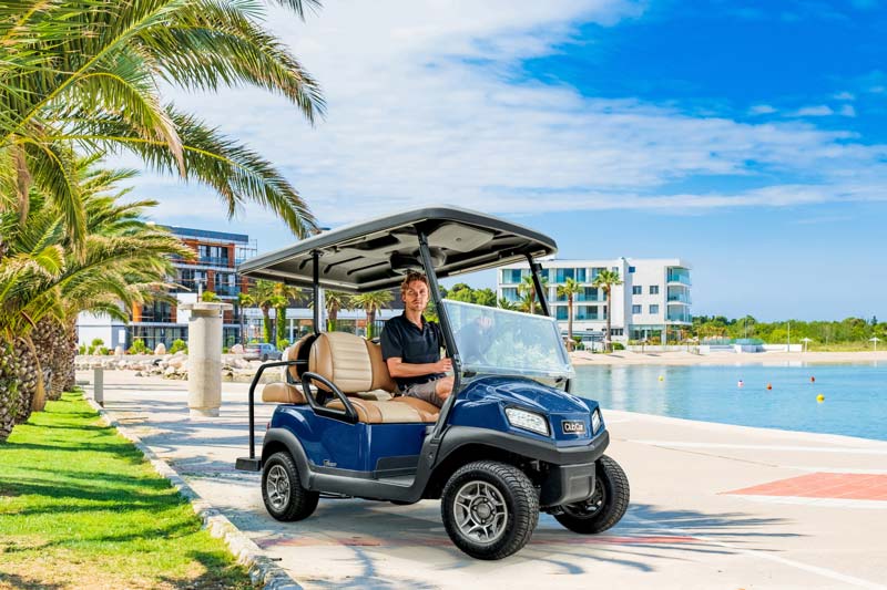 Photo of a CLub Car Tempo 2+2 at a lodge with hotels in the background.