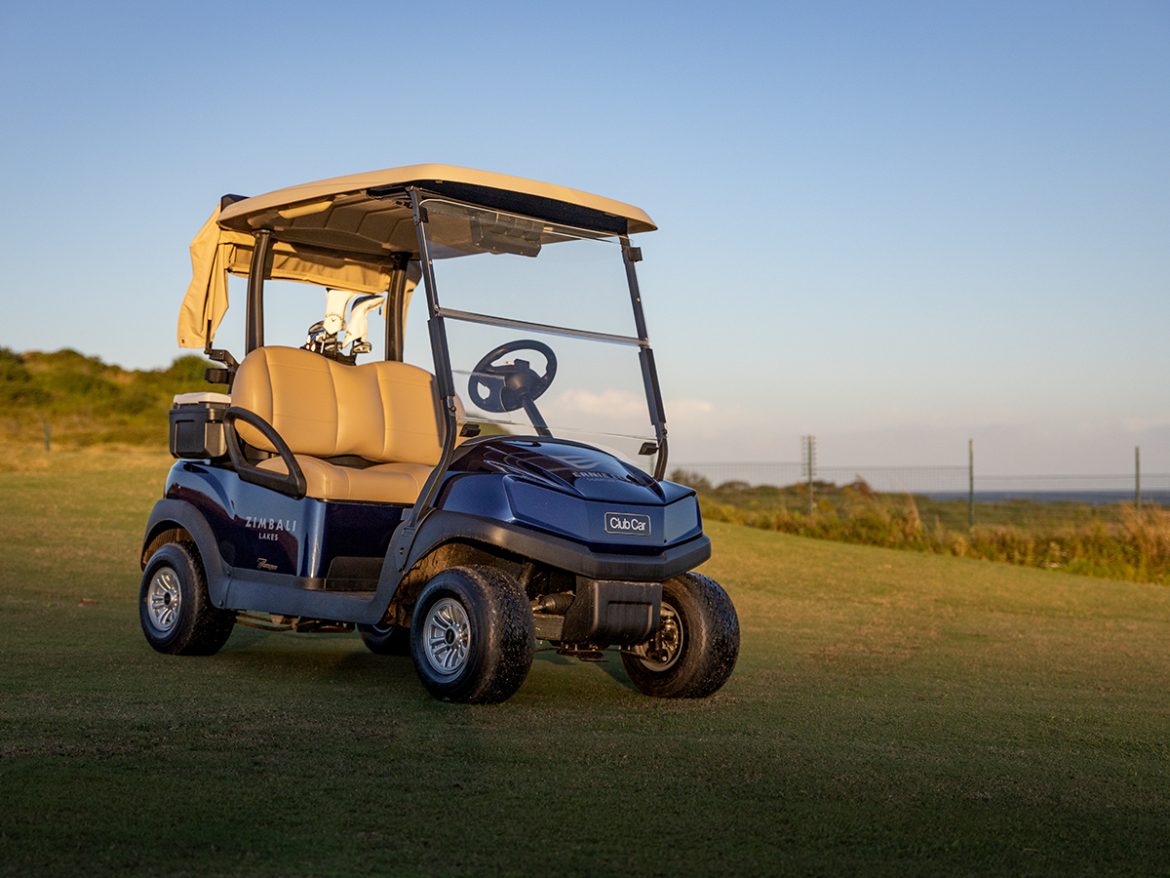 A blue Club Car Tempo parked in the sun on the Zimbali Lakes golf course with a hint of the ocean in the background.