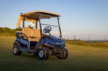 A blue Club Car Tempo parked in the sun on the Zimbali Lakes golf course with a hint of the ocean in the background.