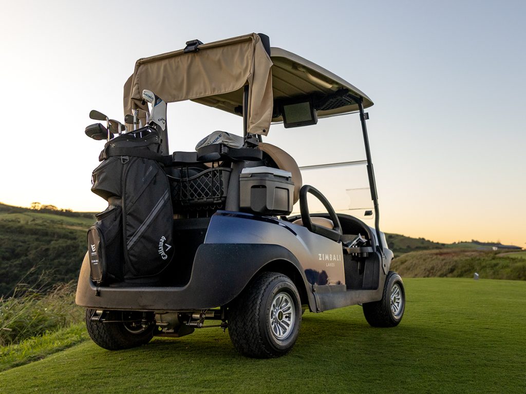 A blue Club Car Tempo parked on the Zimbali Lakes golf course. The golf cart is parked at a 3/4 angle and taken from the photo provides a back view. You can see a golf bag on the back of the golf cart that is held in place by the Club Car Bag Holder accessory.