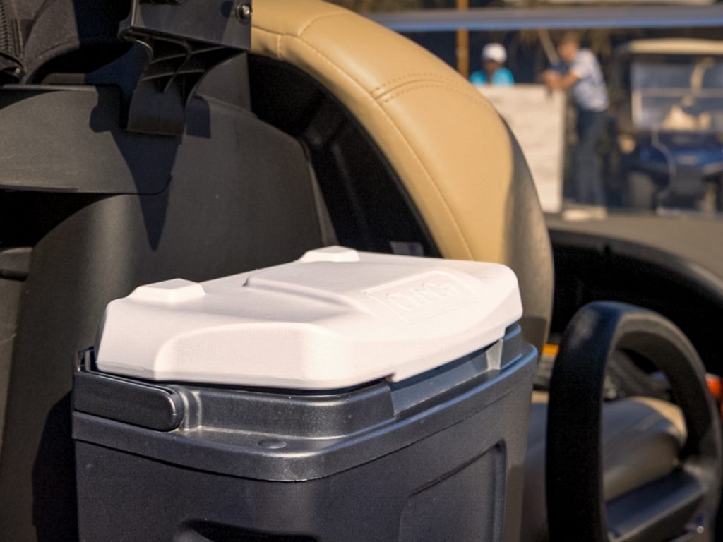 A Club Car Cooler Box accessory attached to the side of a Club Car Tempo. You can see golfers in the background.