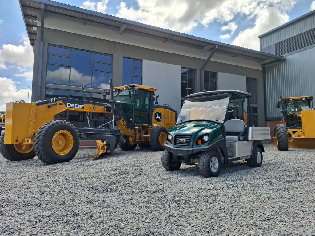 A photo taken of a Club Car Carryall and two John Deere Motor Graders on each side of the Club Car, outside the AFGRI Equipment Gauteng branch.