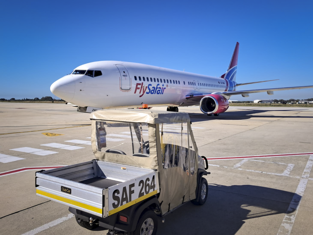 A Club Car Carryall utility vehicle in the foreground at an airport with a FlySafair Boeing in the background