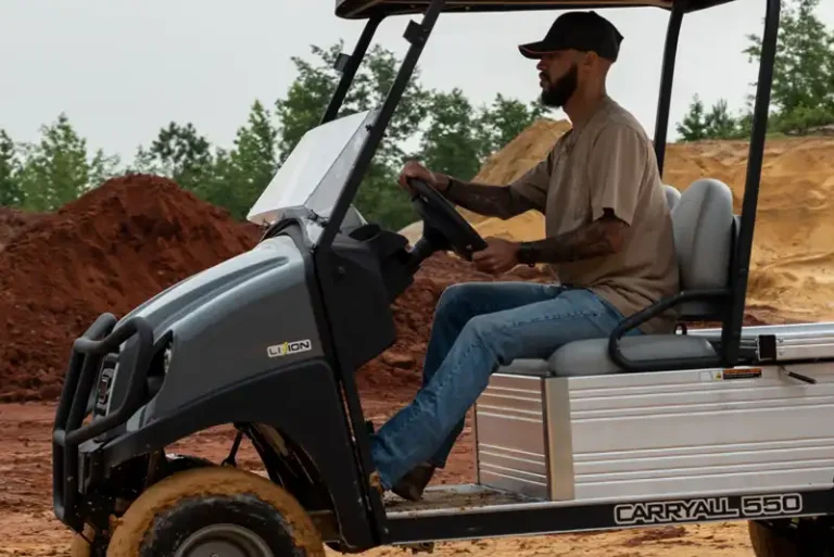 A Club Car Carryal vehicle being driven by a worker to get around a worksite. The wheels are dirty with mu and there is dirt and mud in the background.