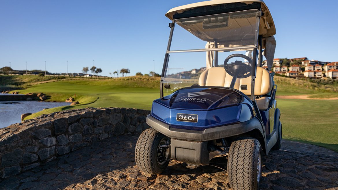 A photo of a Club Car Tempo in blue, parked on a stone bridge at the Zimbali Lakes Ernie Els Signature golf course. You can see the green in the background with a clear, blue sky.