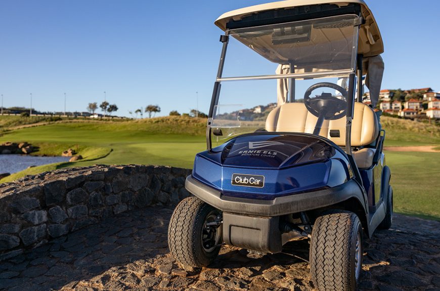 A photo of a Club Car Tempo in blue, parked on a stone bridge at the Zimbali Lakes Ernie Els Signature golf course. You can see the green in the background with a clear, blue sky.