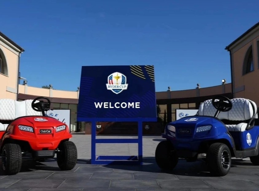 A photo of two Club Cars, one in red and the other in blue, standing at the entrance to the Ryder Cup