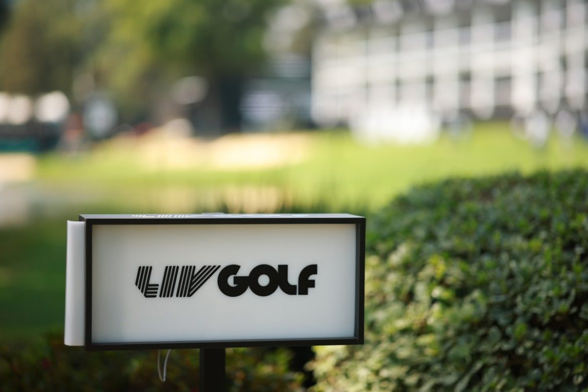 A logo of LIV Golf on a board in front of bushes at a golf course