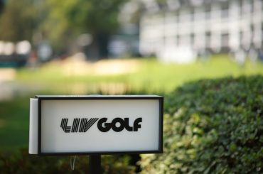 A logo of LIV Golf on a board in front of bushes at a golf course