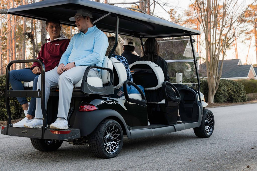 Club Car 6 Passenger vehicle transporting people across a sports facility/estate/hotel ground.
